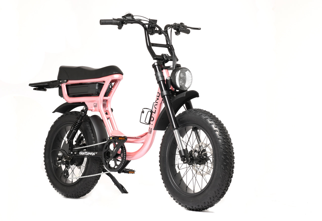 An electric bike with black frame and accessories, including a helmet, chain lock, phone holder, and top bar bag. The bike has large wheels, a rear rack, and an LCD color display.