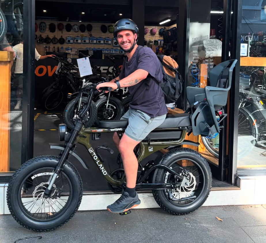 Man posing with a ToLand electric bike in front of a store entrance.